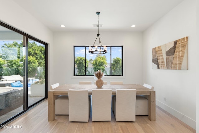 dining area with light hardwood / wood-style floors, a wealth of natural light, and an inviting chandelier