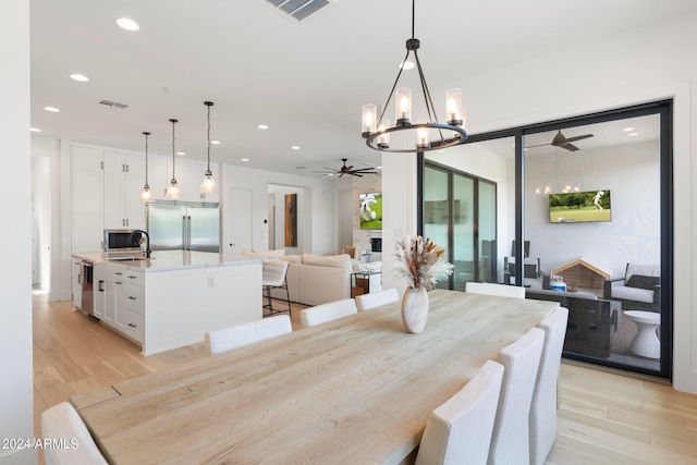 dining space with ceiling fan with notable chandelier, a large fireplace, light hardwood / wood-style flooring, and sink