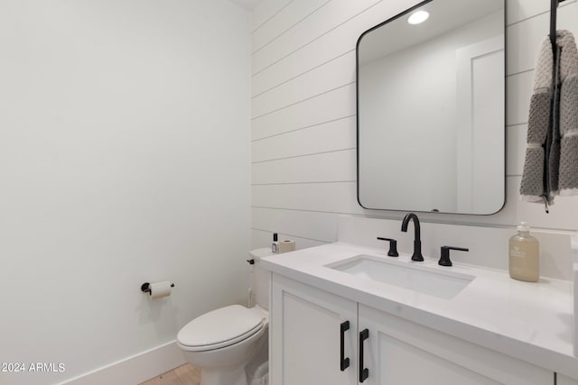 bathroom with vanity, toilet, and wooden walls