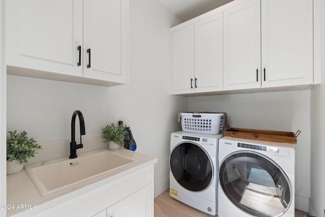 clothes washing area featuring washing machine and clothes dryer, light hardwood / wood-style floors, cabinets, and sink