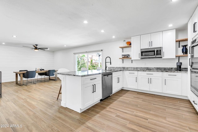 kitchen with dark stone countertops, appliances with stainless steel finishes, kitchen peninsula, and white cabinets