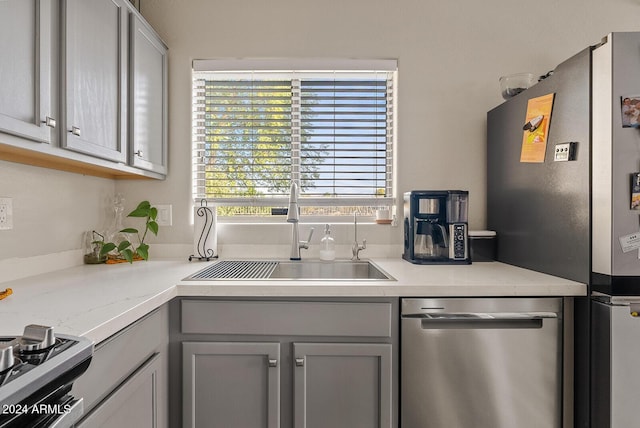 kitchen featuring gray cabinetry, light stone counters, sink, and appliances with stainless steel finishes