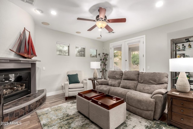 living area featuring visible vents, a glass covered fireplace, wood finished floors, french doors, and ceiling fan