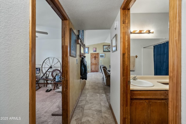 hallway with vaulted ceiling, sink, light tile patterned floors, and a textured ceiling