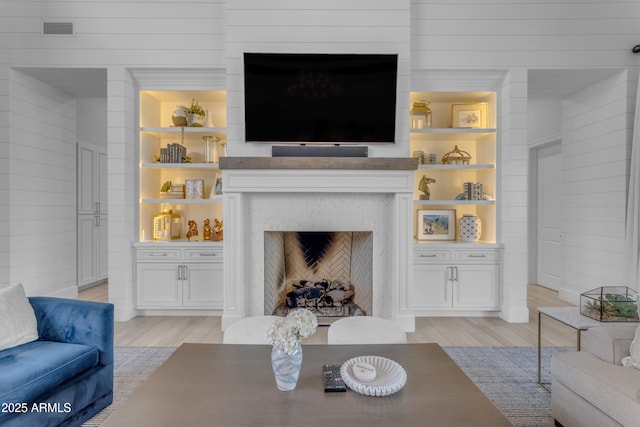 living area with light wood-style floors, wooden walls, a fireplace, and visible vents