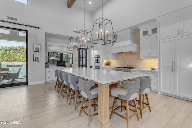 kitchen with tasteful backsplash, premium range hood, visible vents, and white cabinetry