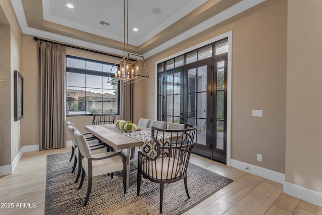 dining room featuring light wood-type flooring, visible vents, a tray ceiling, and baseboards