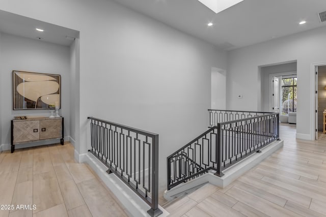 hallway featuring visible vents, a skylight, wood finished floors, and an upstairs landing