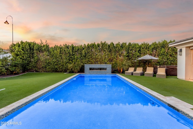 pool at dusk featuring an outdoor pool and a lawn