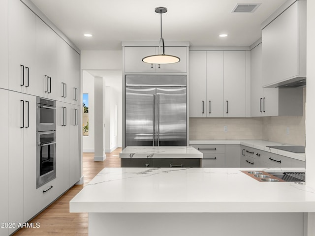 kitchen featuring pendant lighting, backsplash, light stone counters, stainless steel appliances, and light wood-type flooring