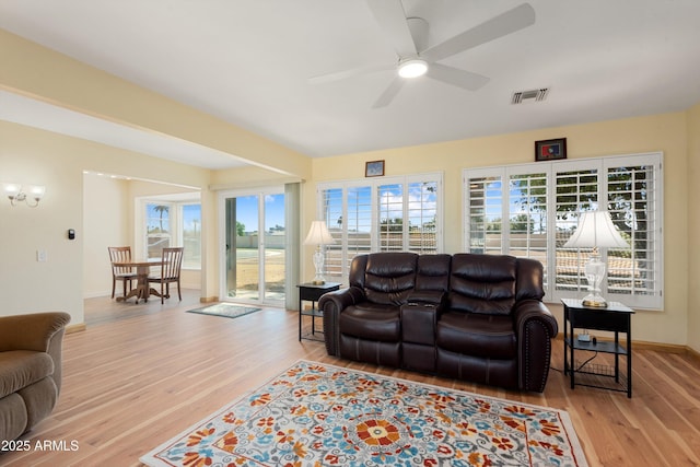 living area with ceiling fan with notable chandelier, wood finished floors, visible vents, and baseboards