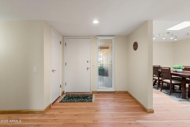 foyer entrance with light wood-style flooring, rail lighting, a skylight, and baseboards