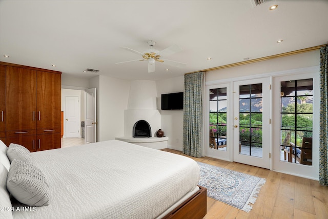 bedroom featuring access to outside, french doors, ceiling fan, light wood-type flooring, and a fireplace