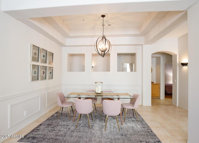 dining area featuring light tile patterned floors, arched walkways, a tray ceiling, a decorative wall, and a notable chandelier