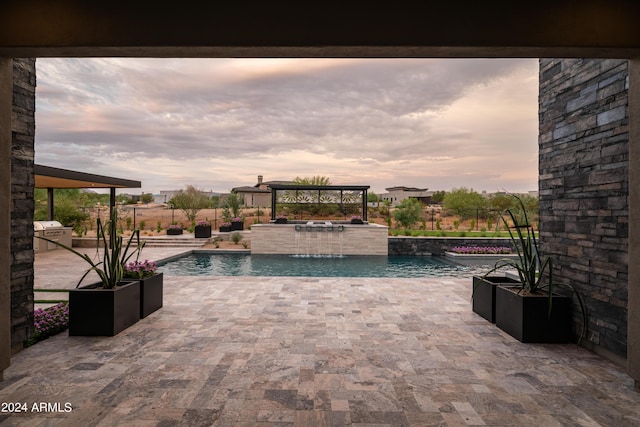 pool at dusk featuring a patio area, a hot tub, and pool water feature