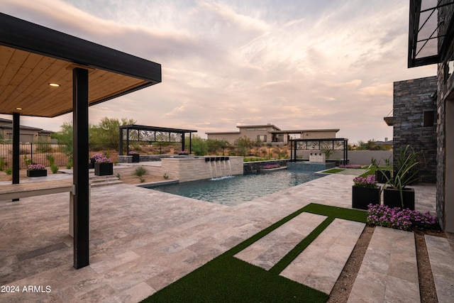 pool at dusk with a gazebo, a patio area, pool water feature, and an in ground hot tub