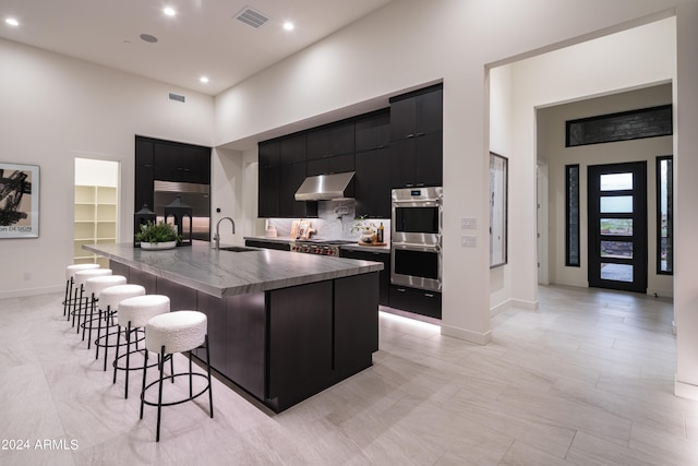 kitchen with sink, a breakfast bar area, a towering ceiling, stainless steel double oven, and a large island