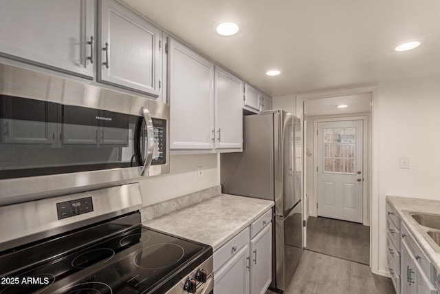 kitchen featuring appliances with stainless steel finishes, light countertops, wood finished floors, recessed lighting, and a sink