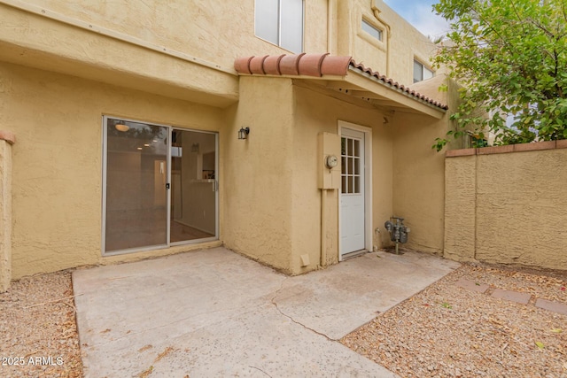 entrance to property with stucco siding, a patio, fence, and a tiled roof