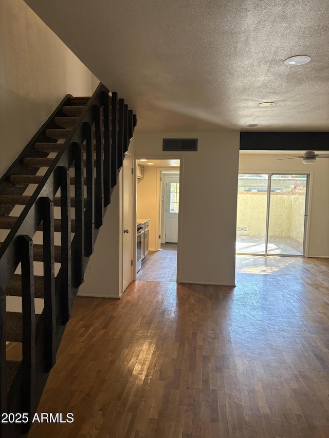 unfurnished living room featuring plenty of natural light, stairs, wood finished floors, and a textured ceiling