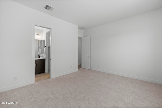 unfurnished bedroom featuring light carpet and ensuite bath