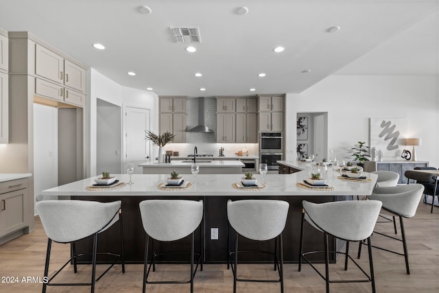 kitchen featuring wall chimney exhaust hood, light hardwood / wood-style floors, a breakfast bar area, stainless steel double oven, and a spacious island