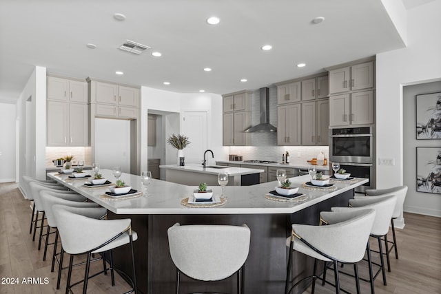 kitchen featuring wall chimney exhaust hood, light hardwood / wood-style flooring, a kitchen breakfast bar, backsplash, and a spacious island