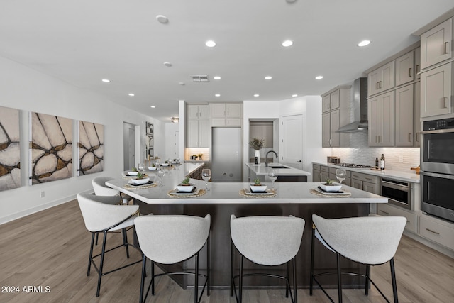 kitchen featuring a large island, light wood-type flooring, a kitchen breakfast bar, and wall chimney range hood