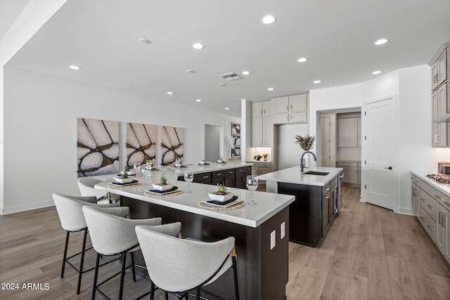 kitchen with light wood-type flooring, a kitchen island with sink, a breakfast bar, sink, and kitchen peninsula