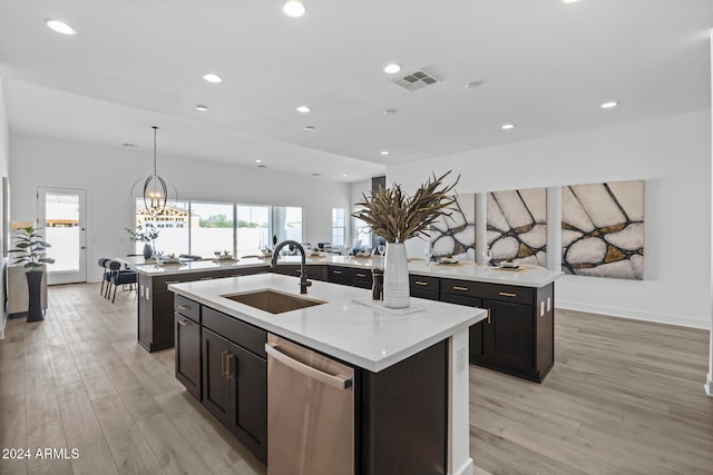 kitchen with a kitchen island with sink, a chandelier, light wood-type flooring, sink, and stainless steel dishwasher