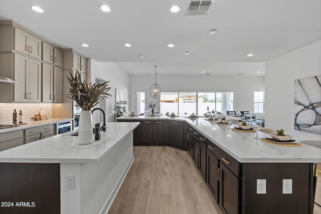 kitchen with light wood-type flooring, decorative light fixtures, light stone counters, stainless steel appliances, and a spacious island