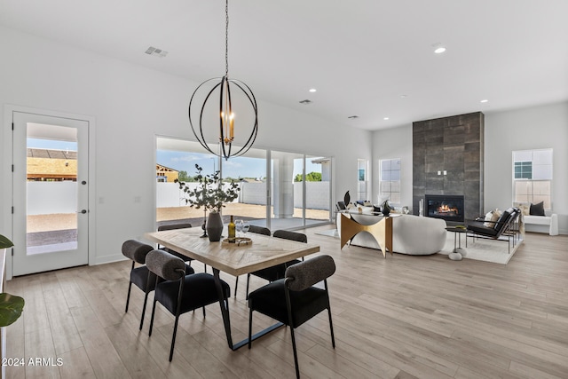 dining space featuring a tile fireplace, a chandelier, and light hardwood / wood-style flooring