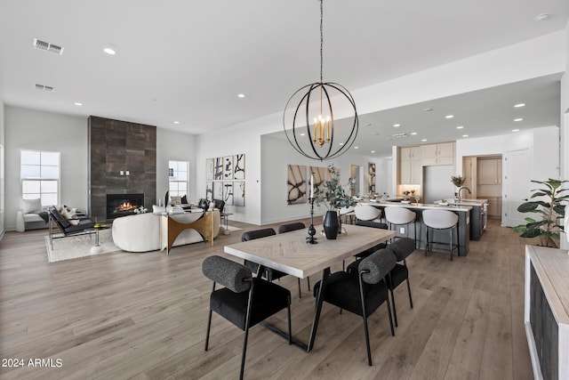 dining area featuring an inviting chandelier, light wood-type flooring, a tiled fireplace, and a wealth of natural light