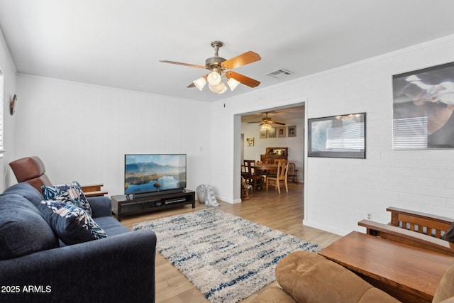 living room with light hardwood / wood-style flooring, ceiling fan, and brick wall