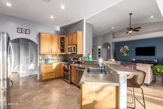 kitchen with stainless steel appliances, sink, kitchen peninsula, vaulted ceiling, and a kitchen breakfast bar