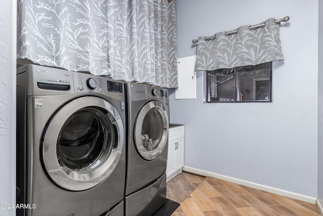 clothes washing area featuring washing machine and dryer, light wood-type flooring, and cabinets