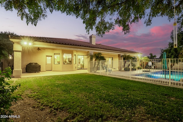 back house at dusk featuring a yard, a fenced in pool, and a patio area