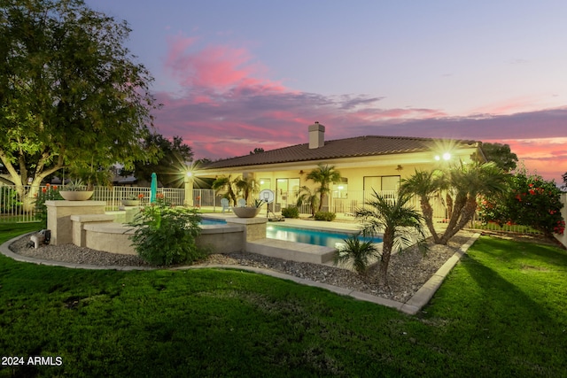 pool at dusk featuring a lawn and a patio area