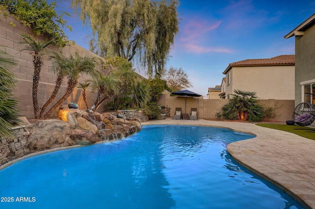 pool at dusk with a patio area and pool water feature