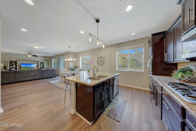 kitchen with hanging light fixtures, sink, dark brown cabinets, stainless steel appliances, and a center island with sink