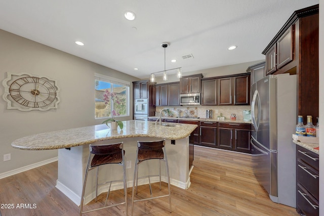 kitchen with hanging light fixtures, sink, backsplash, stainless steel appliances, and light stone counters