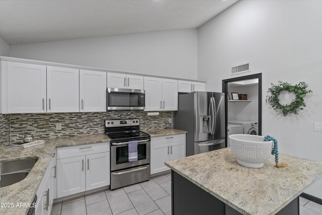 kitchen with white cabinetry, lofted ceiling, appliances with stainless steel finishes, and washer and clothes dryer