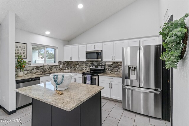 kitchen featuring sink, appliances with stainless steel finishes, white cabinetry, light stone counters, and a kitchen island