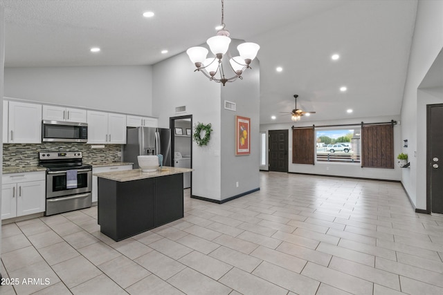 kitchen featuring white cabinetry, light stone counters, decorative light fixtures, appliances with stainless steel finishes, and a kitchen island