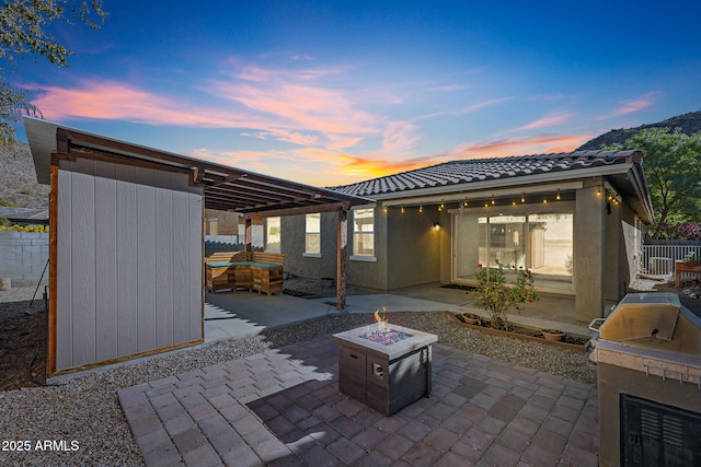 patio terrace at dusk featuring an outdoor fire pit and an outdoor kitchen