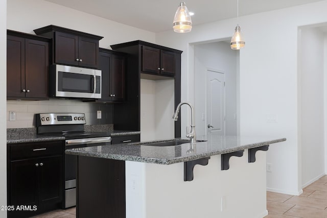 kitchen featuring a center island with sink, appliances with stainless steel finishes, hanging light fixtures, sink, and backsplash