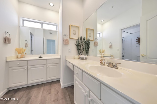 full bathroom featuring two vanities, wood finished floors, baseboards, and a sink