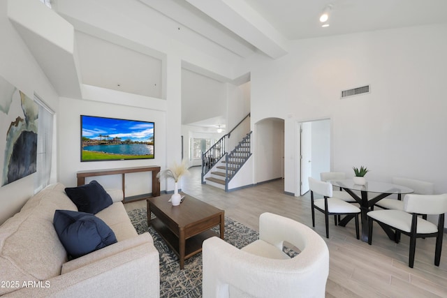 living area featuring light wood-style flooring, stairway, visible vents, arched walkways, and a towering ceiling