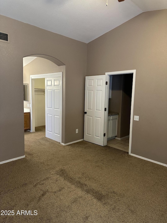 unfurnished bedroom with a closet, a spacious closet, ensuite bath, vaulted ceiling, and light carpet