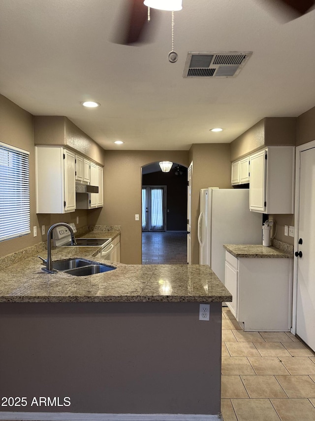 kitchen featuring white fridge, sink, a healthy amount of sunlight, kitchen peninsula, and white cabinets